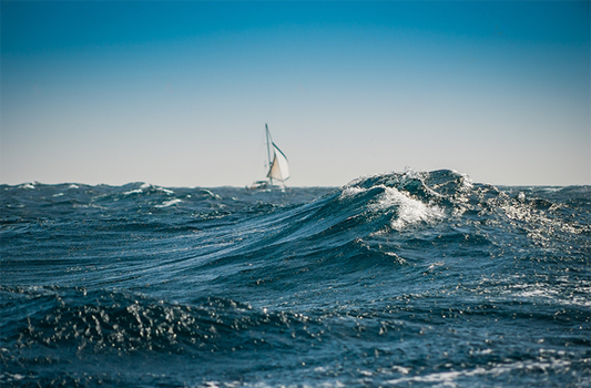 A breaking wave with sailboat passing SY Alegria whilst doing the Atlantic Crossing in a big swell with wind, on a day with blue sky